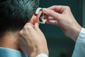 Doctor or audiologist professionally fitting a new open-fit hearing aid device on a patient.