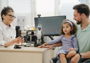 Dallas audiologist examining a young girl's hearing, with her father present for pediatric consultation.