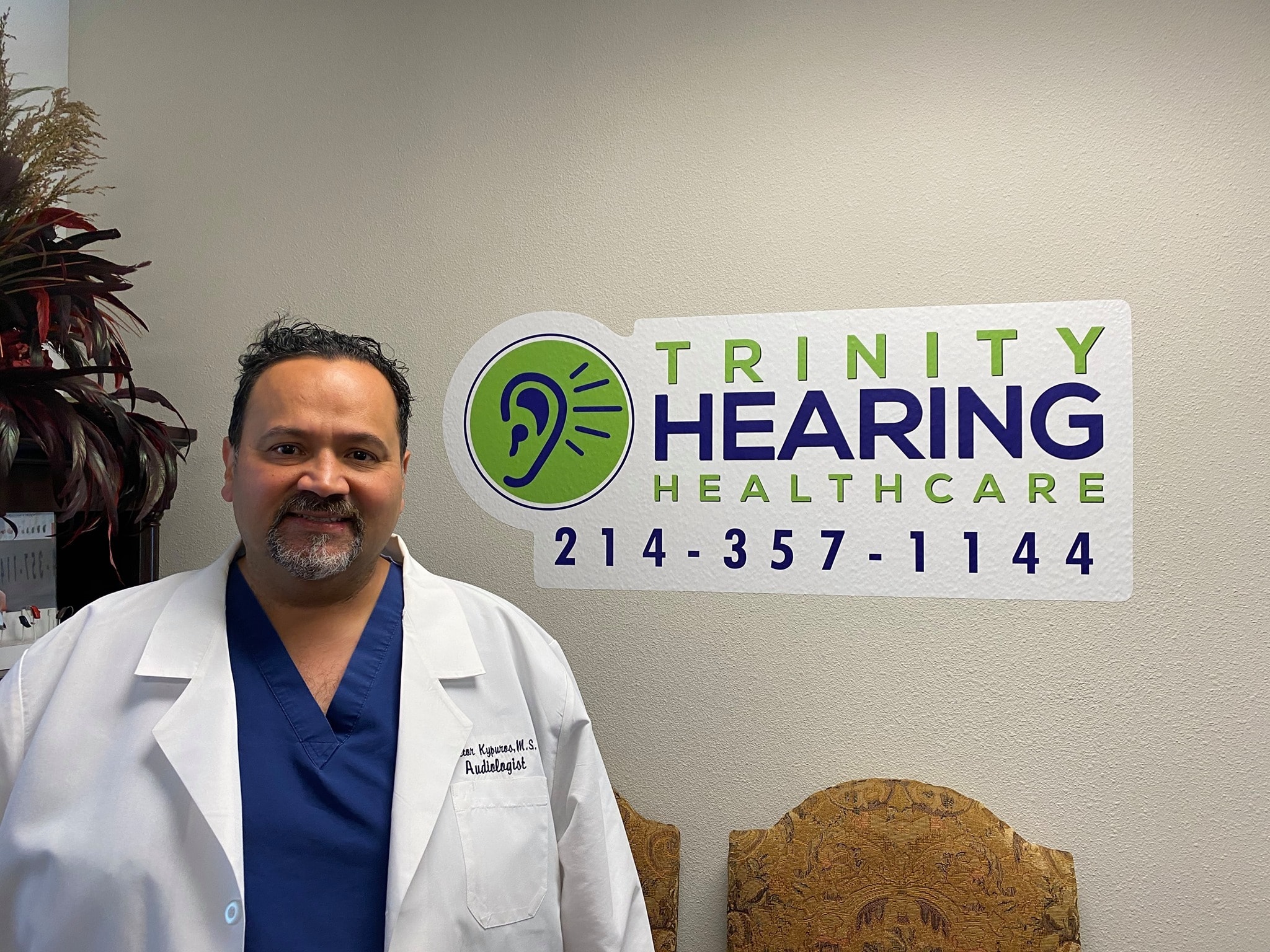 Dr. Hector Kypuros, the expert audiologist at Trinity Hearing Healthcare, in front of the clinic logo.