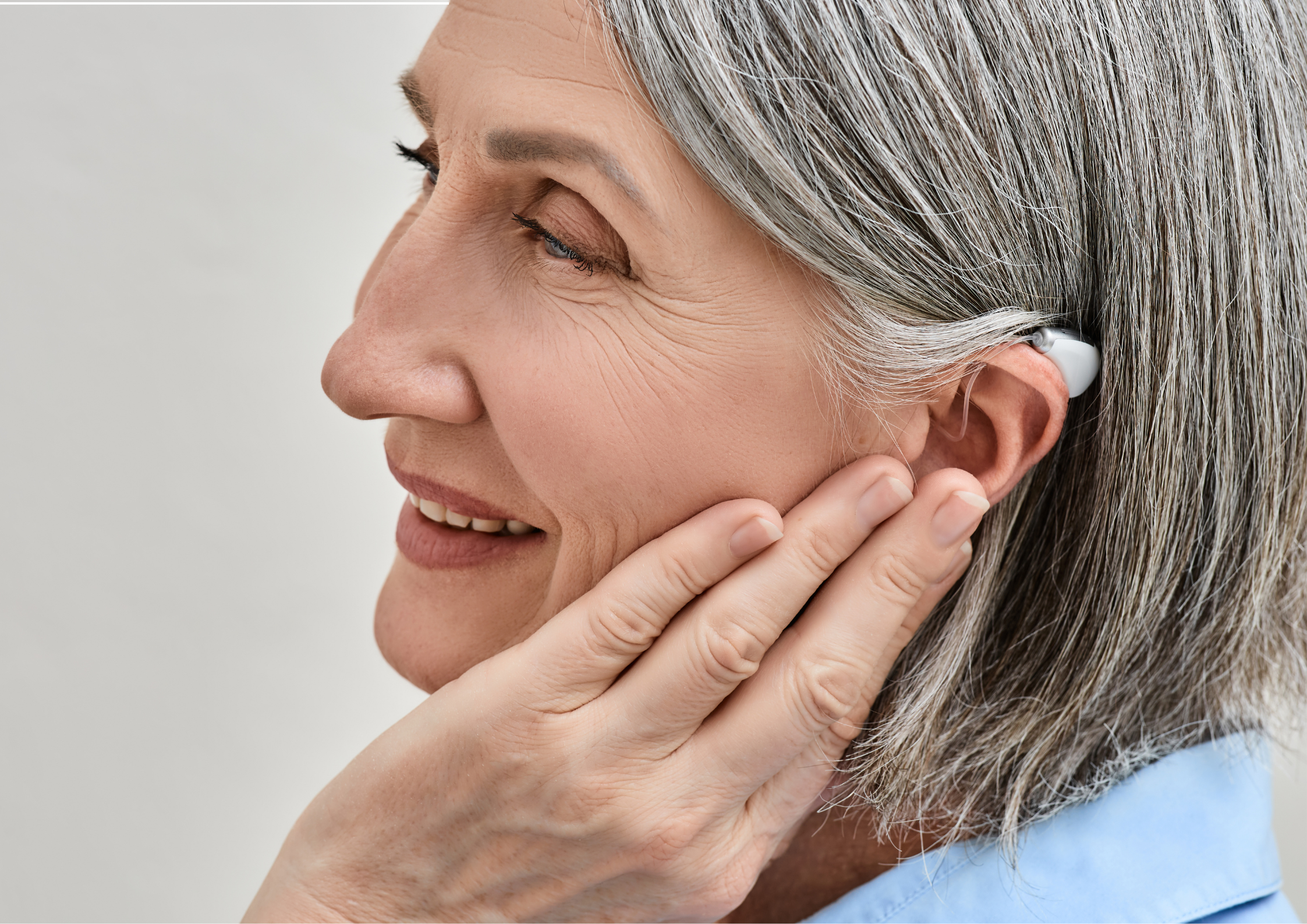 Senior woman successfully inserting her new in-the-ear (ITE) hearing aid.