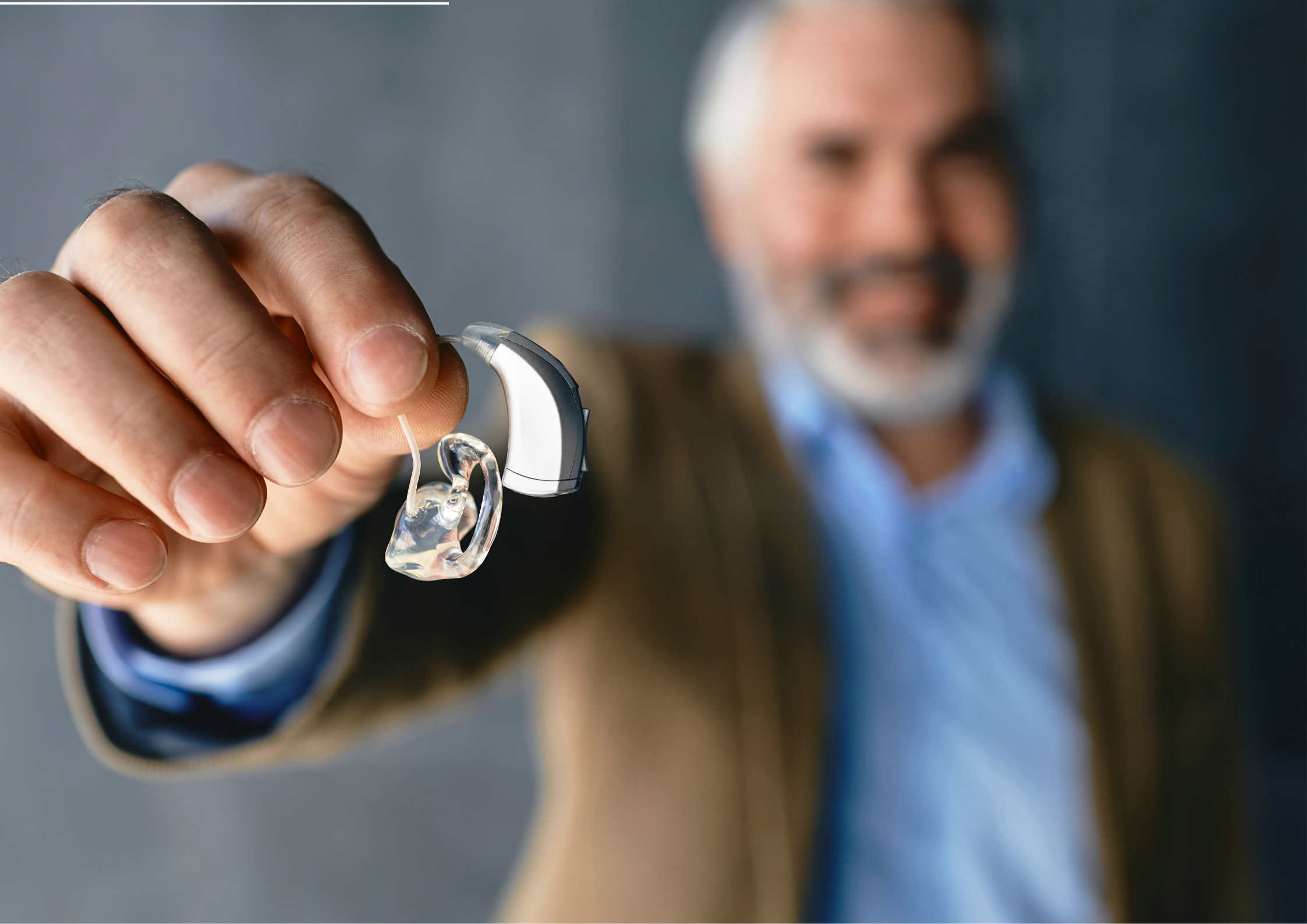 Audiologist holding up a modern, small digital hearing aid device for close inspection.