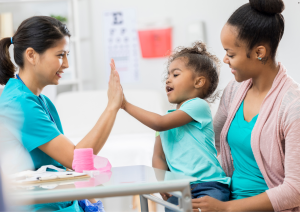 Pediatric audiologist giving a high-five to a young girl after a successful hearing checkup.