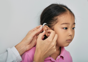 Audiologist fitting a small hearing aid on a child, specializing in pediatric hearing evaluations.
